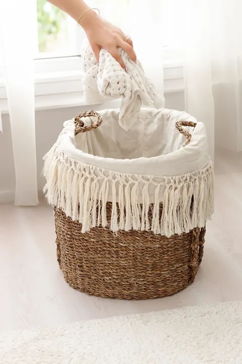 A hand placing laundry in a wicker basket beside a window.