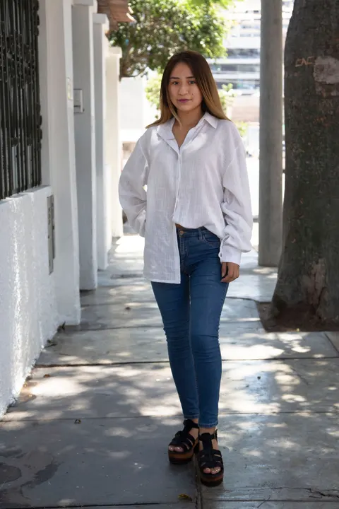 A woman in a white shirt and jeans standing on a city sidewalk.