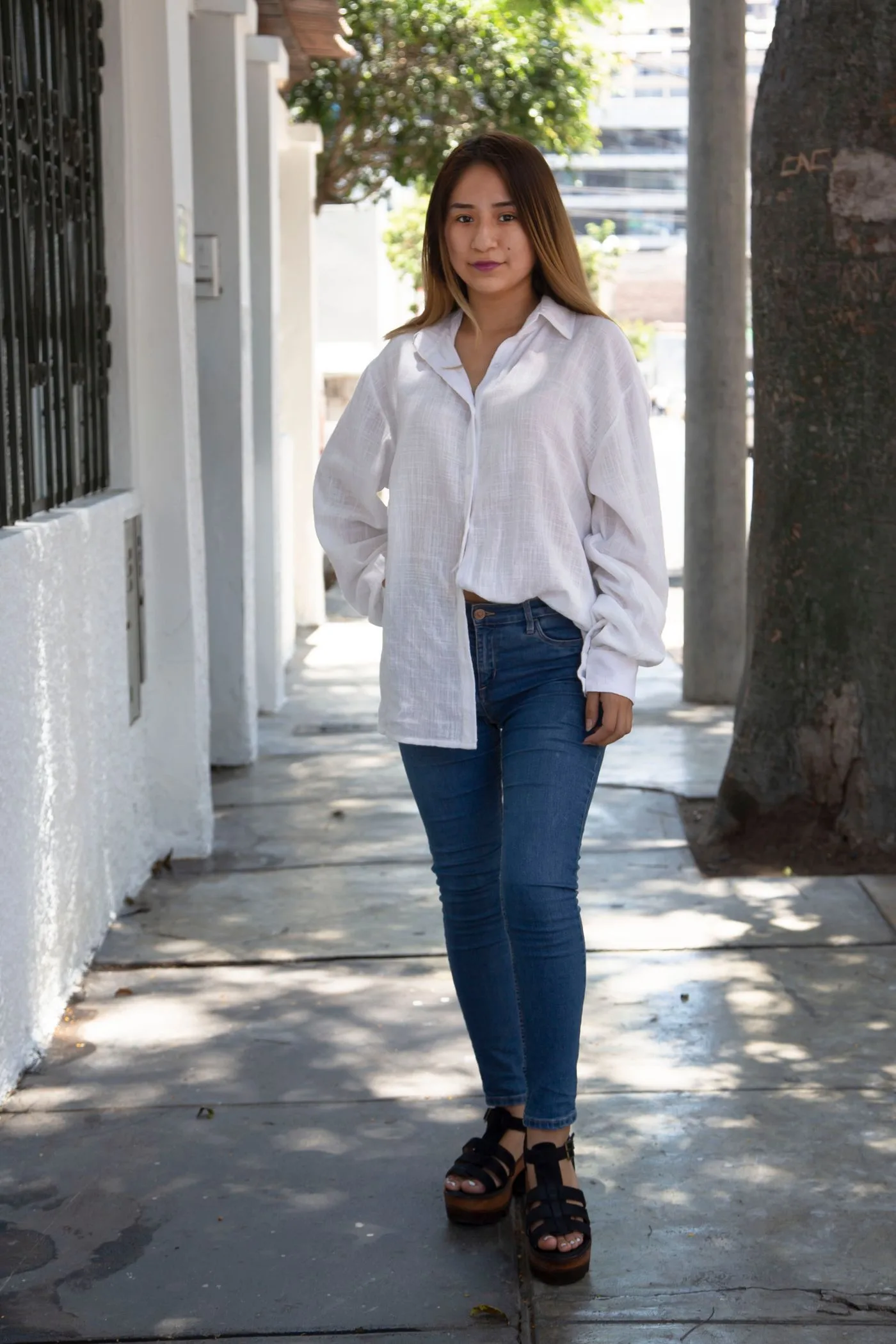 A woman in a white shirt and jeans standing on a city sidewalk.